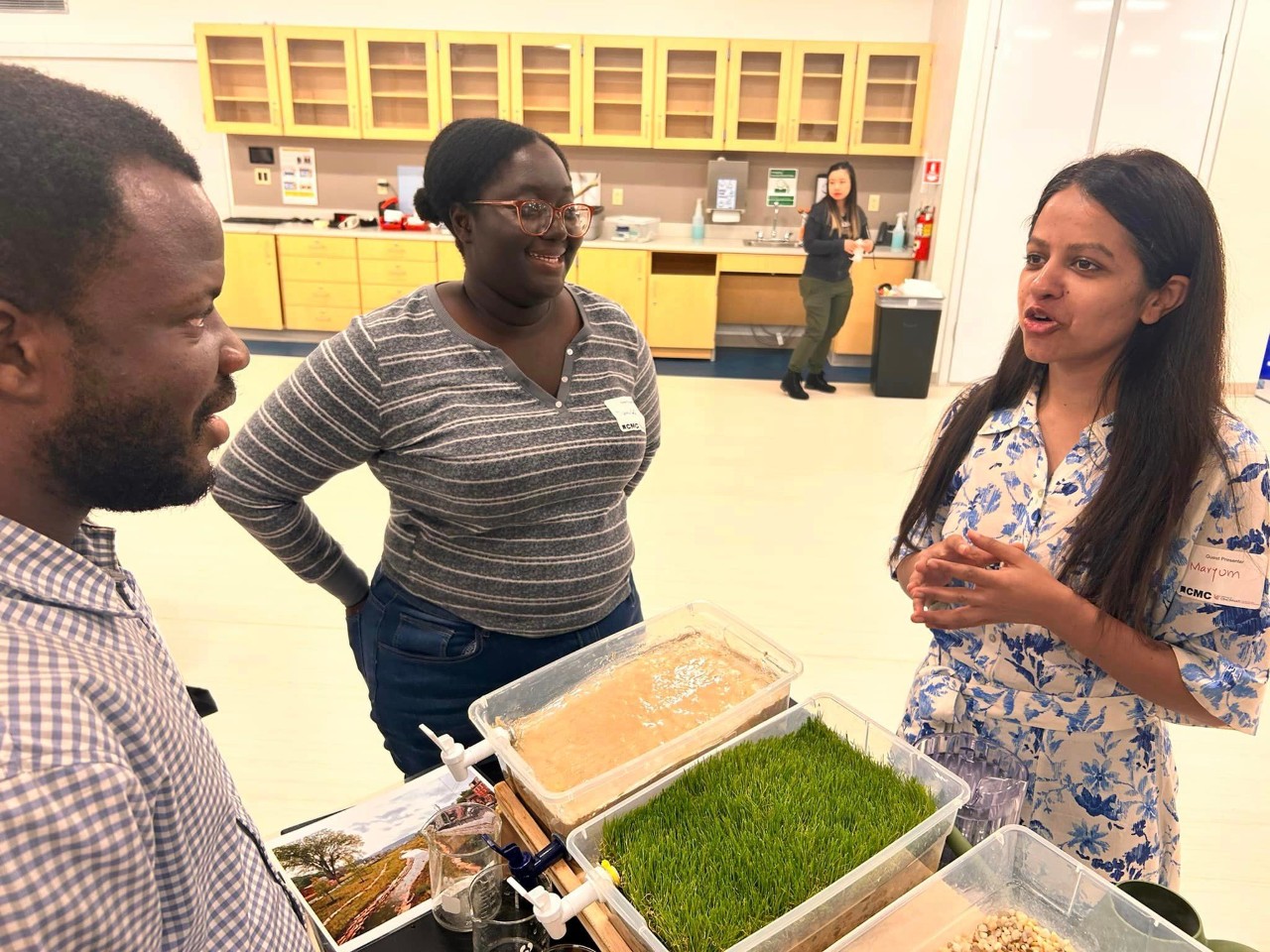 Three students stand around a table, smiling.