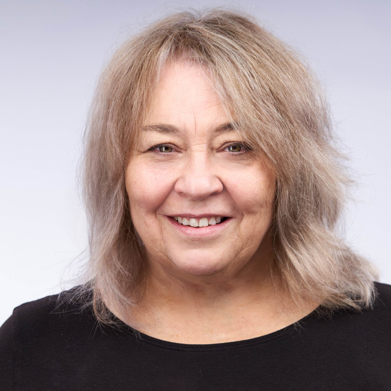 A color photograph of Abeba Birhane wearing glasses, earrings, and a necklace with a silver collared shirt in front of a blue background.