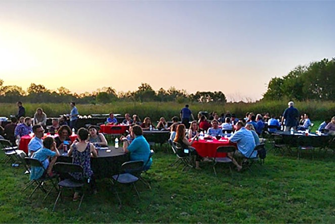 Conference attendees of Sensorium 2017 attend an outdoor banquet seated at round tables on a grassy field.