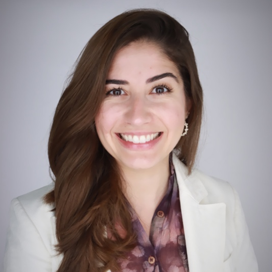 A color photo of Valeria Andrade smiling and wearing a white suit and a purple shirt.