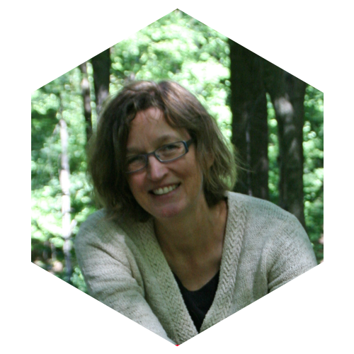 Hexagon shaped Photo of Lora Arduser outside in the woods with green leaves and trees behind her, Image links to Faculty and social media page