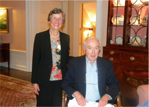 A woman, standing, and man in wheelchair, smiling at camera