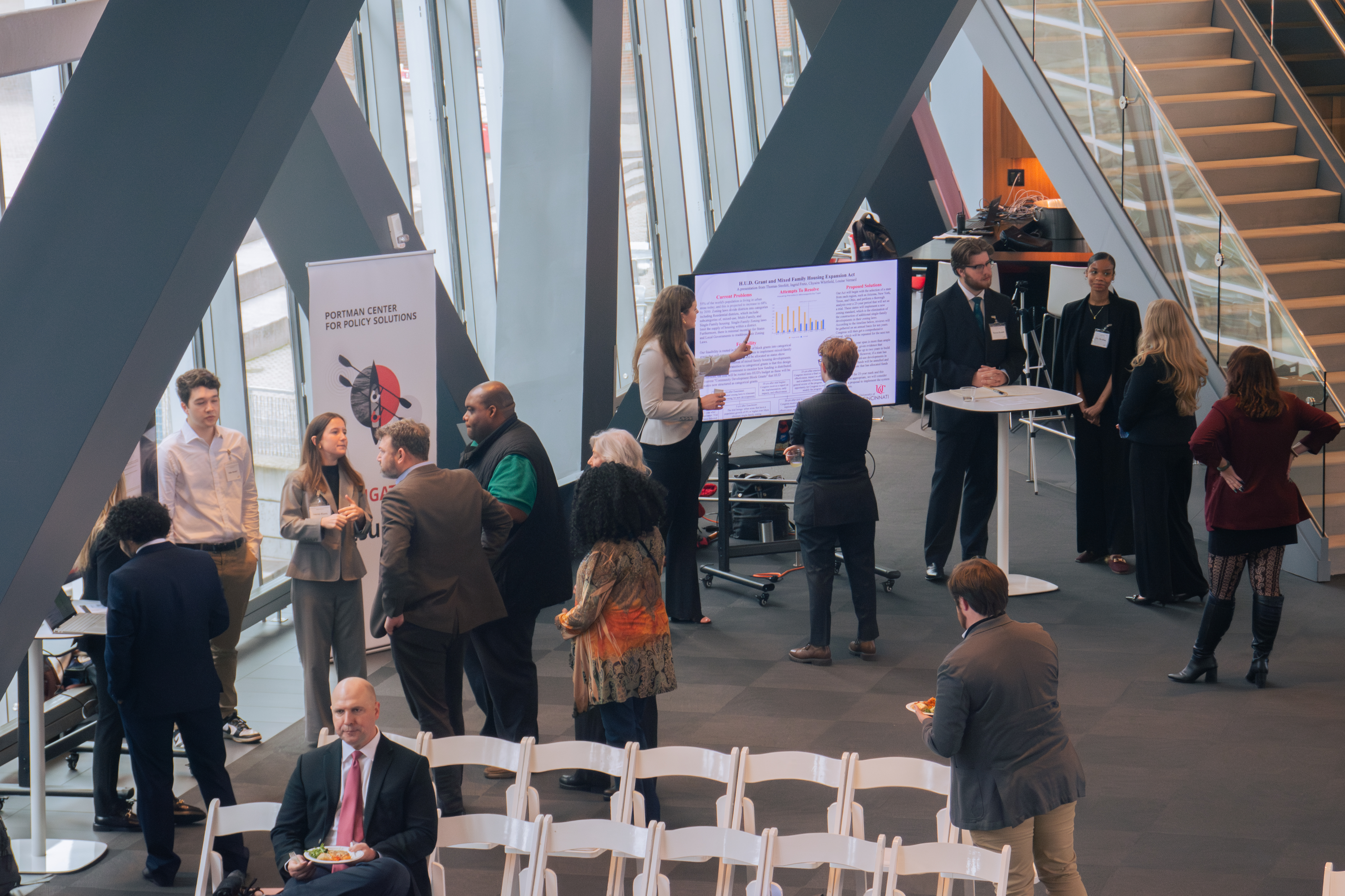 A modern conference room with people networking around presentation boards. Attendees are engaged in discussions, creating a professional and dynamic atmosphere.