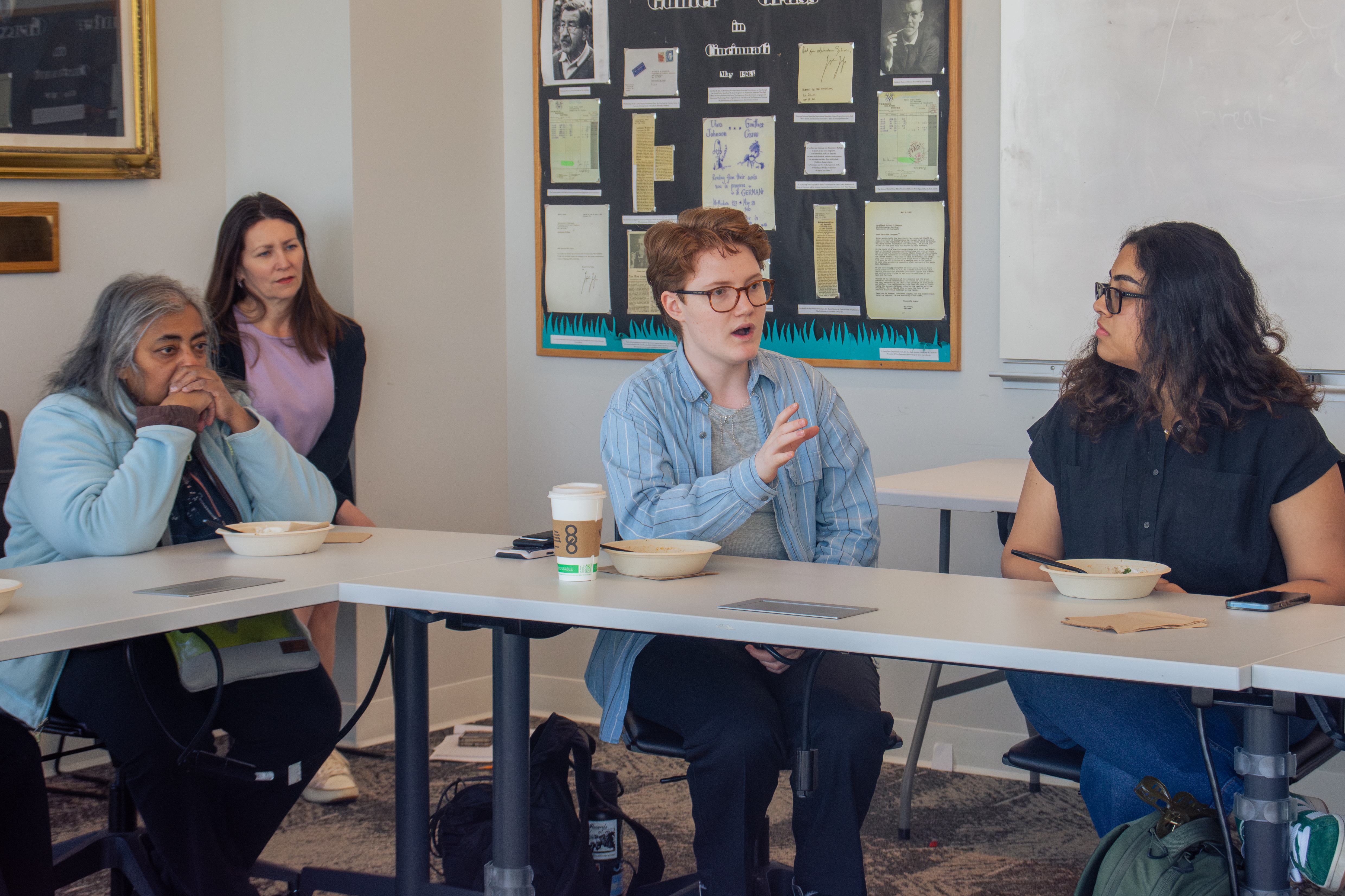 A group of four people sit around a table in a discussion, with one person gesturing animatedly. The atmosphere is engaged and focused.