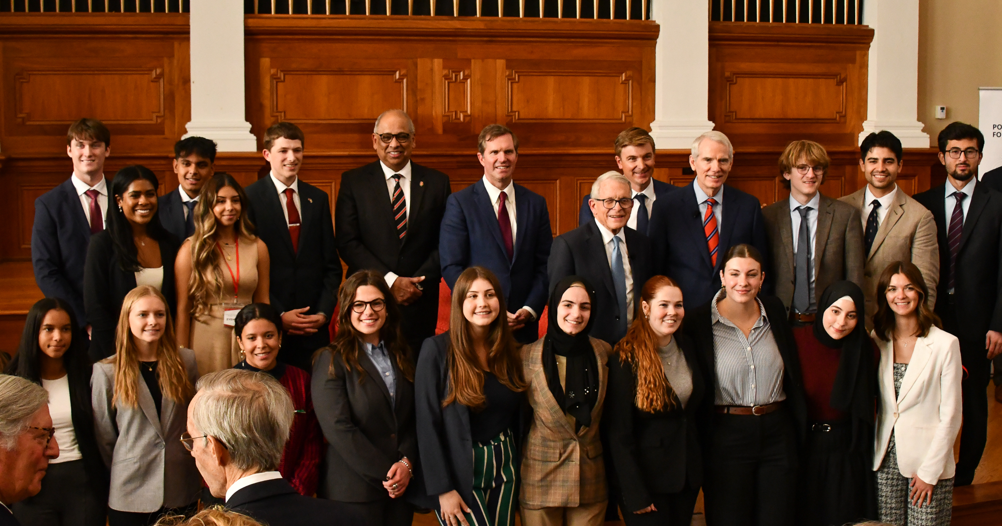 A diverse group of people in formal attire pose for a photo in a wood-paneled room, conveying a sense of accomplishment and professionalism.