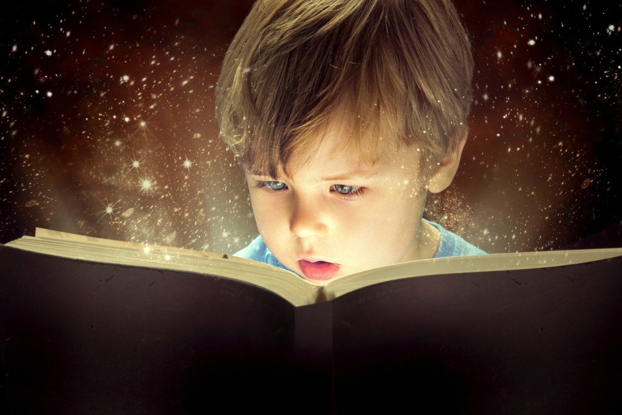 Child reading book that has light coming out of it